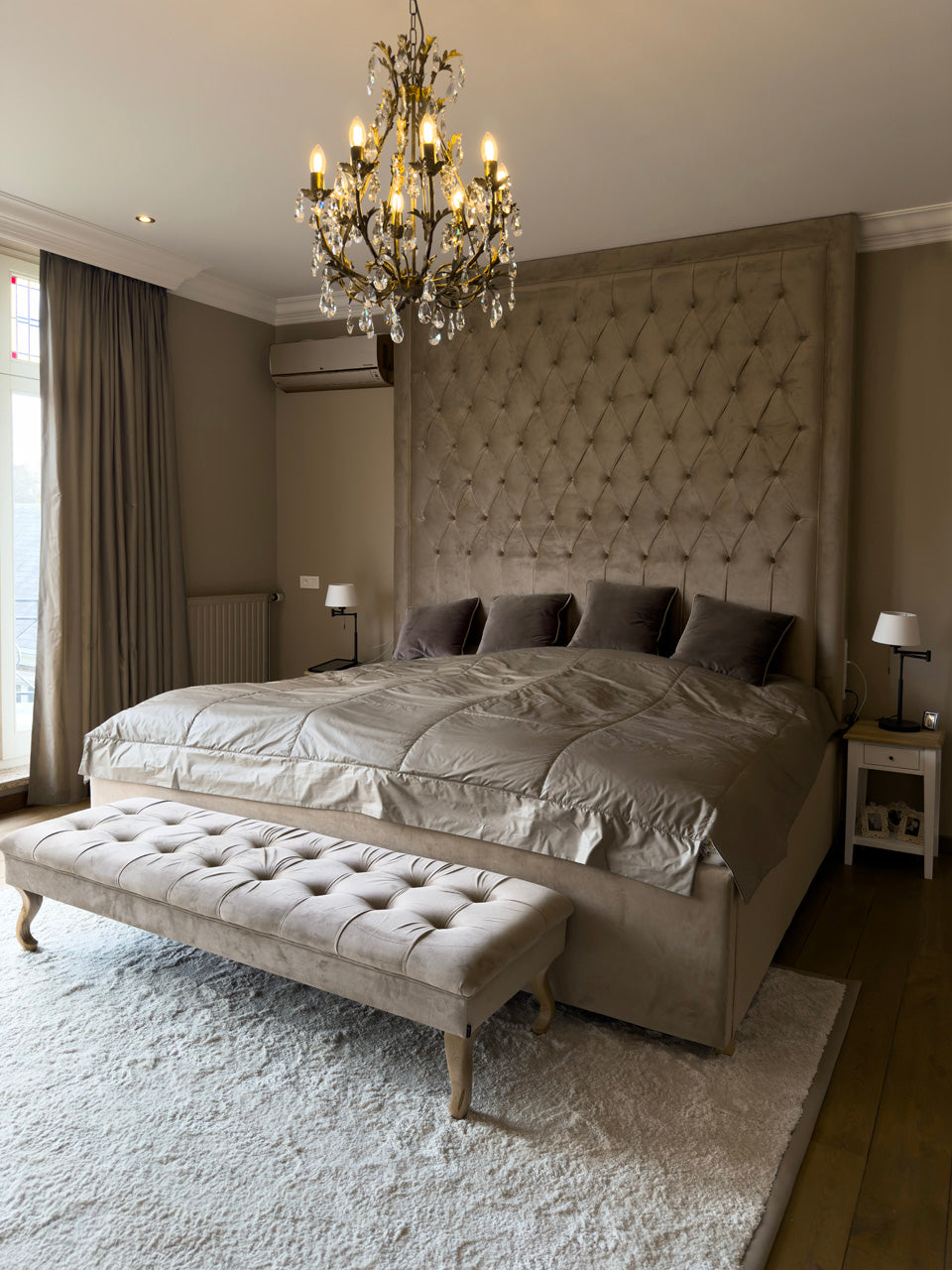 Restful bedroom with a tufted headboard, crystal chandelier and an upholstered bench