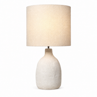 Front view of the Oskar 1916E table lamp mit its 1xE27 bulb illuminated, casting a soft warm glow through the textured white shade. The white sand finish and 31 cm tall silhouette deliver atmospheric, refined lighting for modern living rooms and bedrooms, by Marcottestyle.