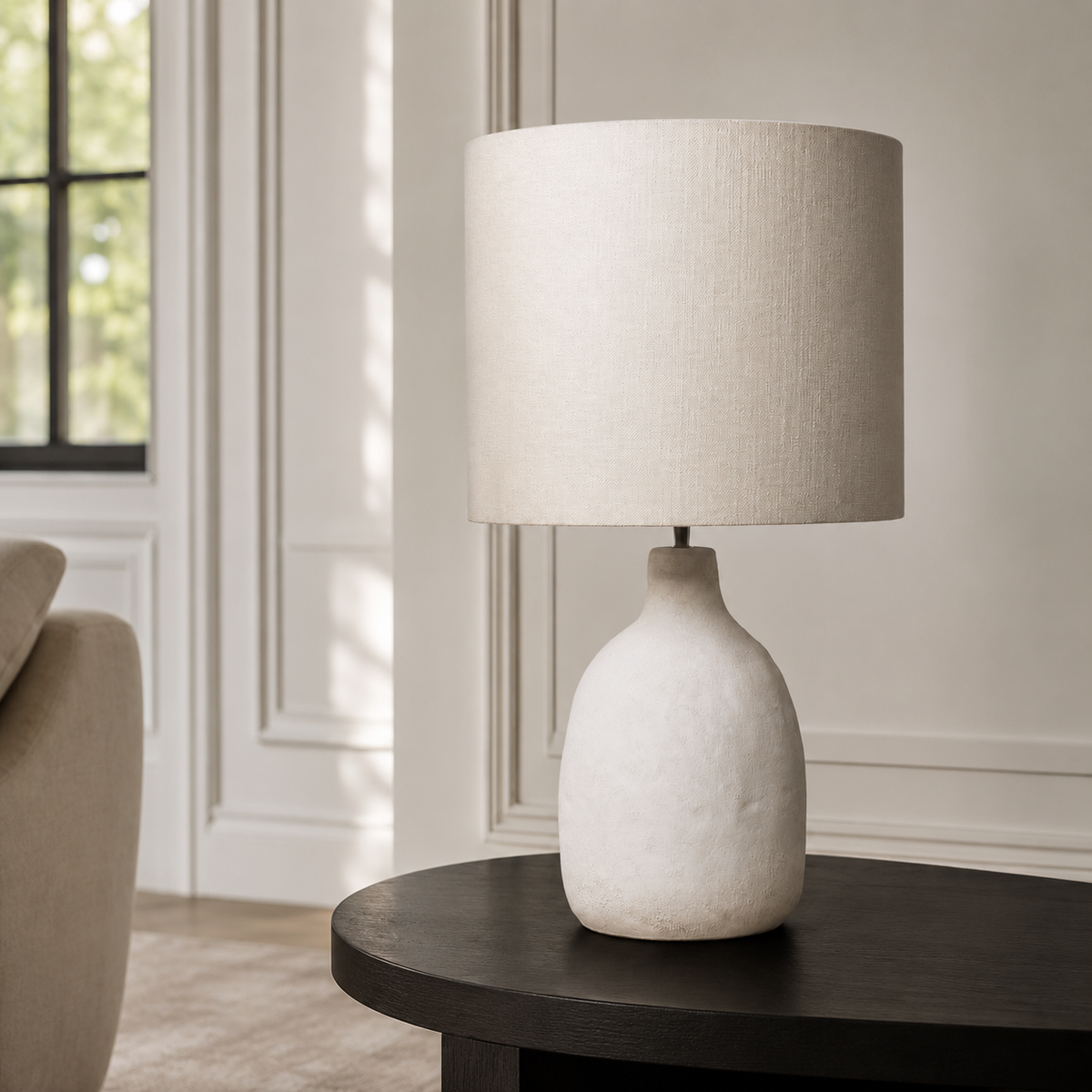 In-room lifestyle view of the Oskar 1916E table lamp placed on a console in a modern living room with classic framing and velvet carpet, harmonised with soft sunlight reflections. A 31 cm tall white 1xE27 table lamp for refined contemporary interiors, by Marcottestyle.