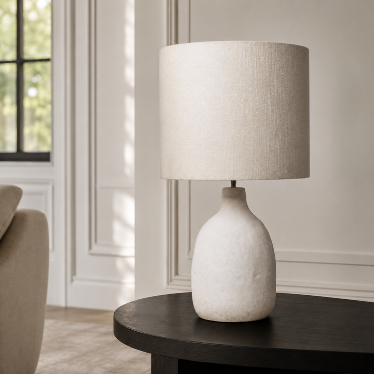 In-room lifestyle view of the Oskar 1916E table lamp placed on a console in a modern living room with classic framing and velvet carpet, harmonised with soft sunlight reflections. A 31 cm tall white 1xE27 table lamp for refined contemporary interiors, by Marcottestyle.