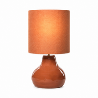 Tischlampe Stella 2575R mit light turned on, warm glow softly visible through fabric shade, rustic terracotta ceramic base on white background, professional product photography by Marcottestyle